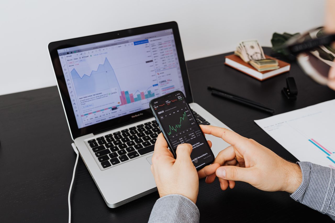 testimonial-img Person analyzing stock market data on a laptop and smartphone indoors.